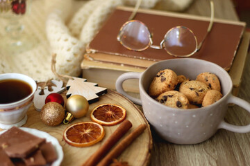 Cup of tea or coffee, various sweets and spices, Christmas decorations, comfy blanket, books and glasses. Selective focus.