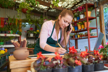 Female florist with smartphone notes order in flower shop