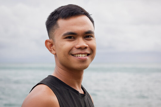 Smiling portrait of young Filipino man by the sea on cloudy day. Asian male model concept