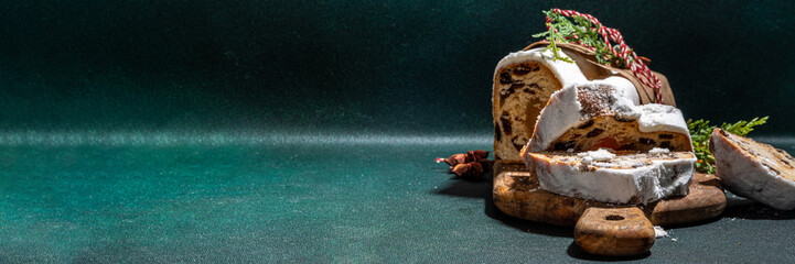  Traditional Christmas Dresdner stollencake with dried fruits, spices, Christmas tree and decoration on dark green concrete background 
