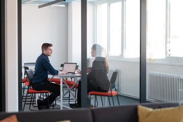 Successful young female leader in a suit with a pink shirt sitting in a modern glass office with a determined smile.