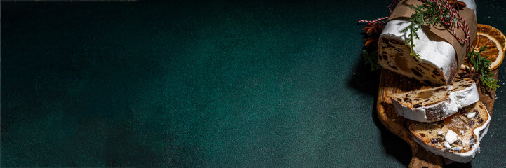  Traditional Christmas Dresdner stollencake with dried fruits, spices, Christmas tree and decoration on dark green concrete background 