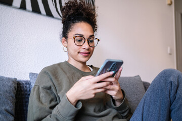 Young black woman using smartphone on sofa