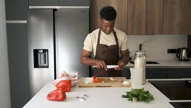 Young african man peeling garlic to prepare chicken recipe in a kitchen.