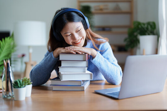 Portrait of young beautiful Asian woman showing smiling face during early morning online class with books, headphones and computer as study materials at home