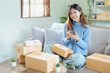Fototapeta na wymiar Starting small business entrepreneur of independent Asian woman smiling using computer laptop with cheerful success of online marketing package box items and SME delivery concept