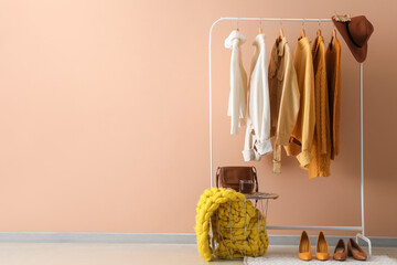 Rack with knitted sweaters, hat and shoes near beige wall in room