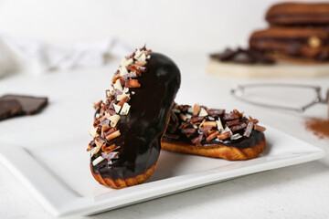 Plate with tasty chocolate eclairs on light table, closeup