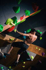 A young, athletic guy with a beautiful inflated body climbs a bouldering in a climbing hall. Emotions on the face.