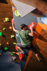 A young, athletic guy with a beautiful inflated body climbs a bouldering in a climbing hall....