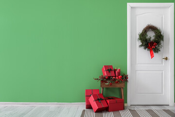 White door with Christmas wreath, presents and candles on table near green wall