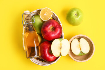 Basket with bottle of apple cider vinegar and fruits on yellow background