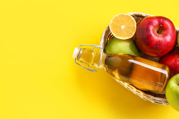 Basket with bottle of apple cider vinegar and fruits on yellow background