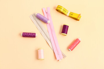 Thread spools, measuring tape and zippers on color background