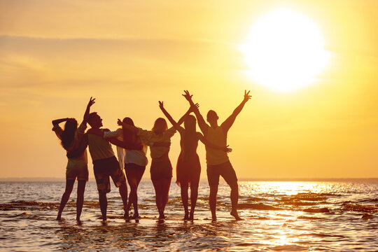 Group of happy young friends are having fun and embracing at sunset beach