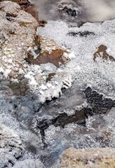 Winter landscape with snow-covered rocks and grass on the river bank
