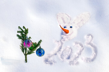 A snowman rabbit with a carrot nose is painted on the snow. Animal zodiac drawing consists of numbers 2023. Symbol of 2023 Chinese New Year. The concept of celebrating Christmas and New Year