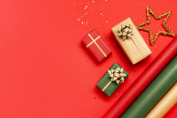 Composition with Christmas gifts, decor and rolls of wrapping paper on red background