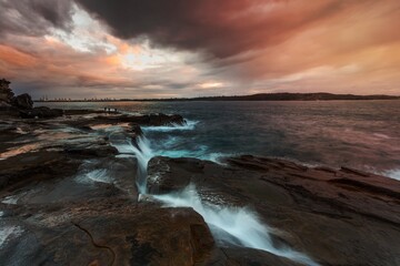 Waves surge up though a deep narrow chasm in rocks near Sydney