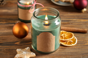 Jar with burning candle and Christmas treats on wooden table, closeup