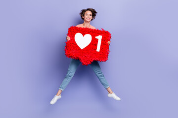 Full length photo of pretty adorable girl dressed orange t-shirt jumping high holding feedback pinata isolated purple color background