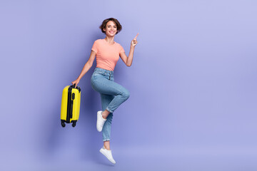 Full length photo of shiny cute lady wear striped t-shirt jumping high holding luggage pointing empty space isolated violet color background