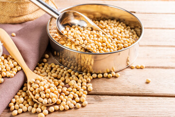 Soybean seeds in wooden bowl with wooden spoon, placed on wooden table, natural healthy food - top view.