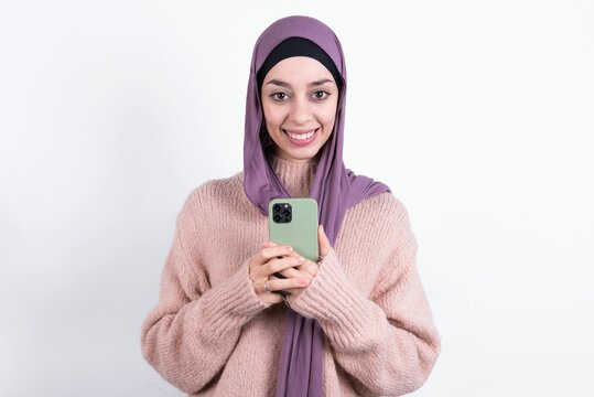 beautiful muslim woman wearing hijab and warm jumper over white background taking a selfie  celebrating success