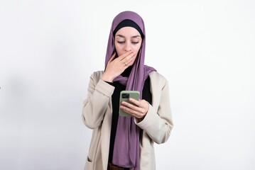 young beautiful muslim woman wearing hijab and jacket over white background being deeply surprised,...