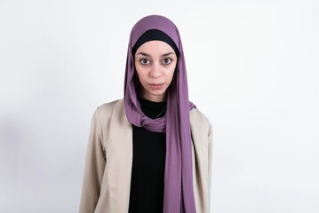 Stunned young beautiful muslim woman wearing hijab and jacket over white background stares reacts on shocking news. Astonished girl holds breath