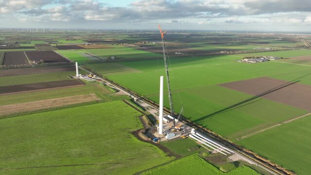 Building process of wind turbine windmill construction with cranes. Parts of the wind turbine, housing, hub, blades on site. Aerial drone overhead. Technical installation