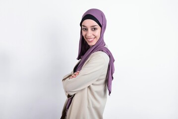 Portrait of young beautiful muslim woman wearing hijab and jacket over white background standing with folded arms and smiling