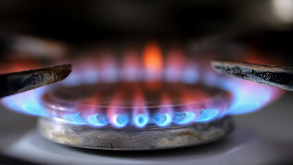 Gas burner with bright red and blue flames on kitchen stove on dark blurred background, closeup