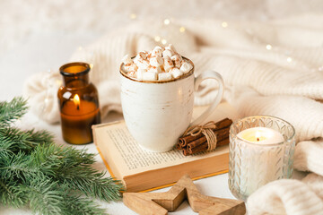 Hygge Cup of hot cocoa or coffee with marshmallow, sweater, candle, book, cinnamon and fir tree. Christmas lights cozy background. Xmas holiday wooden star decorations.