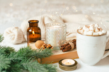 Obraz na płótnie Canvas Hygge Cup of hot cocoa or coffee with marshmallow, sweater, candle, book, cinnamon and fir tree. Christmas lights cozy background. Xmas holiday wooden star decorations.