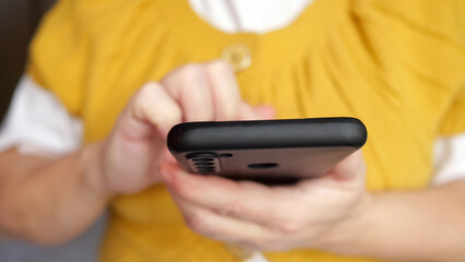 Hand of senior woman typing message to friend on smartphone on blurred background. Female person uses modern electronic device at home closeup