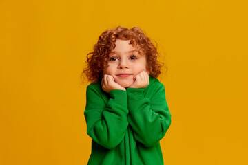 Portrait of cute little girl, child with curly red hair posing isolated over yellow background. Angel face