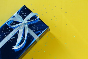 gift in blue wrapping paper with ribbon, yellow background. blue object on a yellow background