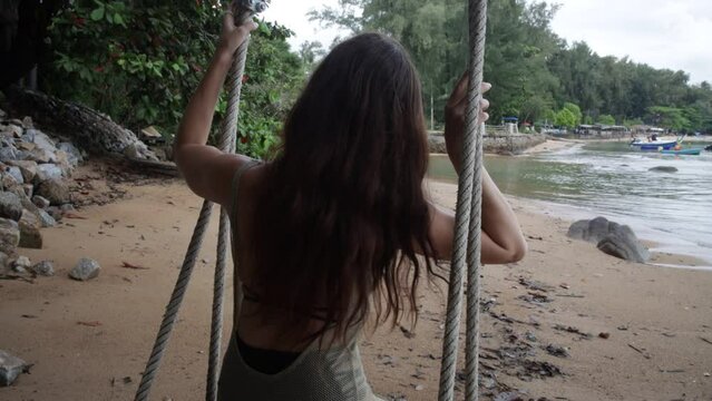 A lonely slender girl relaxes, walks along the beach. a swing on a wild beach