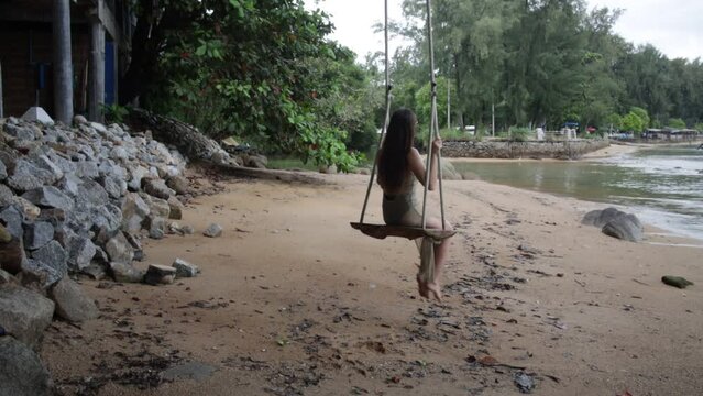 A lonely slender girl relaxes, walks along the beach. a swing on a wild beach
