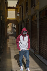 Young man with sunglasses, walking, wearing a two-tone sweatshirt in the street.