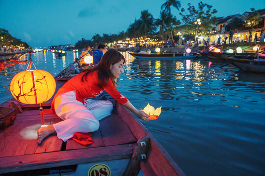 woman wearing Ao Dai Vietnamese dress, traveler Sightseeing Boat Ride and floating paper lantern at Hoi An ancient town. landmark for tourist attractions.Vietnam and Southeast travel concept