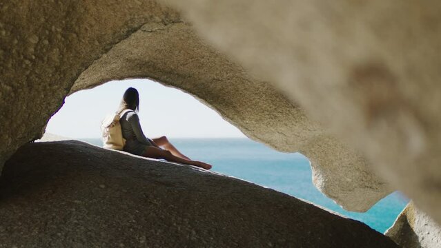 Beach, cave and woman on an adventure on vacation to relax in nature by the seaside in Hawaii. Travel, freedom and girl with a backpack relaxing on rock to explore by ocean on fun holiday or journey.