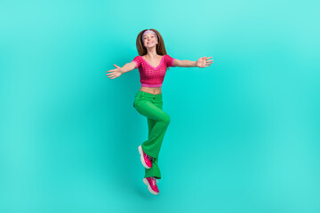 Fototapeta na wymiar Full length photo of pretty charming schoolgirl wear pink crop top flare trousers jumping high open arms isolated turquoise color background