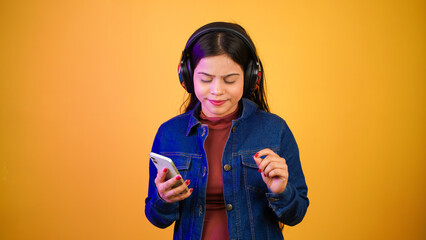 Young woman listening music with wireless headphones on her head, happy teenage girl enjoying music on her mobile phone isolated over colour background
