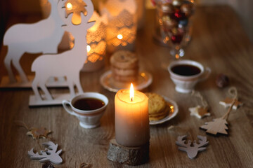Obraz na płótnie Canvas Two types of cookies, cups of tea or coffee, various Christmas decorations and lit candles. Cozy Christmas atmosphere at home. Selective focus.