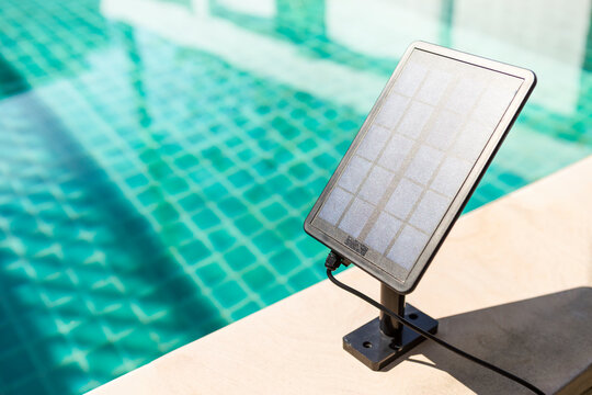 Small solar cell panel on swimming pool edge with space on water surface background, summer outdoor day light, eco technology item, clean energy