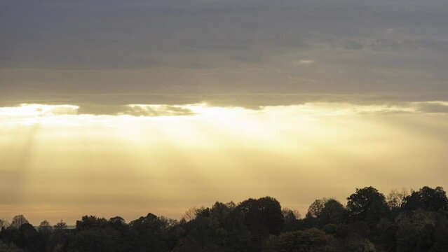 Golden sun rays shining through clouds above a forest time lapse