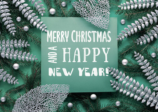 Silver minimal Christmas background with sugar stars and exotic fern leaves on green layered paper background. Caption, Xmas greeting Merry Christmas and a Happy New Year on page.