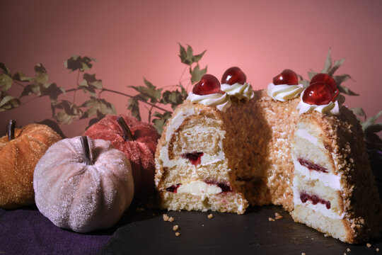 German cake Frankfurter Kranz or Frankfurt Crown Cake. Bisquit with butter cream and cherries. Cut half of the cake. Autumn decor with textile pumpkins and dry leaves.